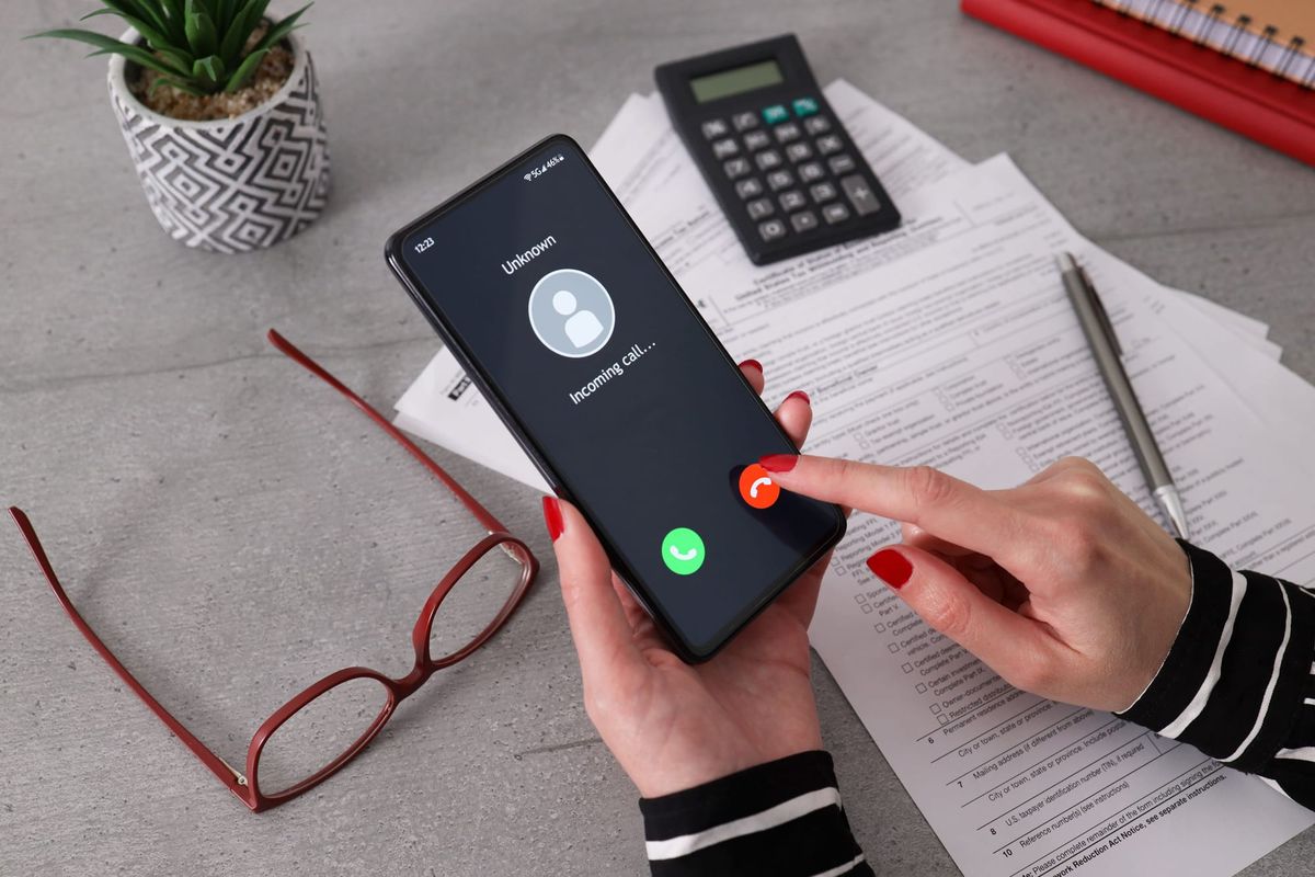 A business owner holds a cell phone with an incoming call from an unknown sender, a red flag for a potential vishing scam