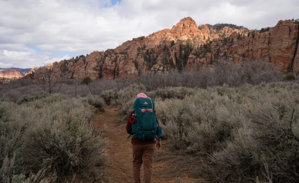 Wide desert canyon landscape with warm evening light, capturing a satellite communicator clipped to a backpack in the foreground.