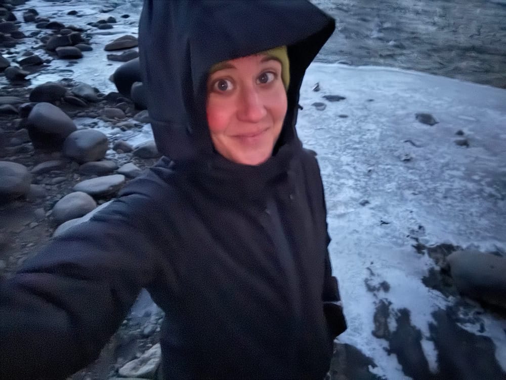 a hiker wearing the paka apu parka with pakafill along a freezing cold river in the mountains in morning