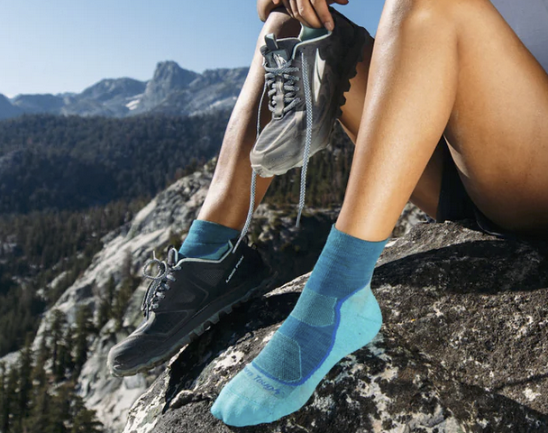 a woman wears 2026 top hiking sock pick darn tough quarter height socks on a mountain hike with a broad vista of high peaks