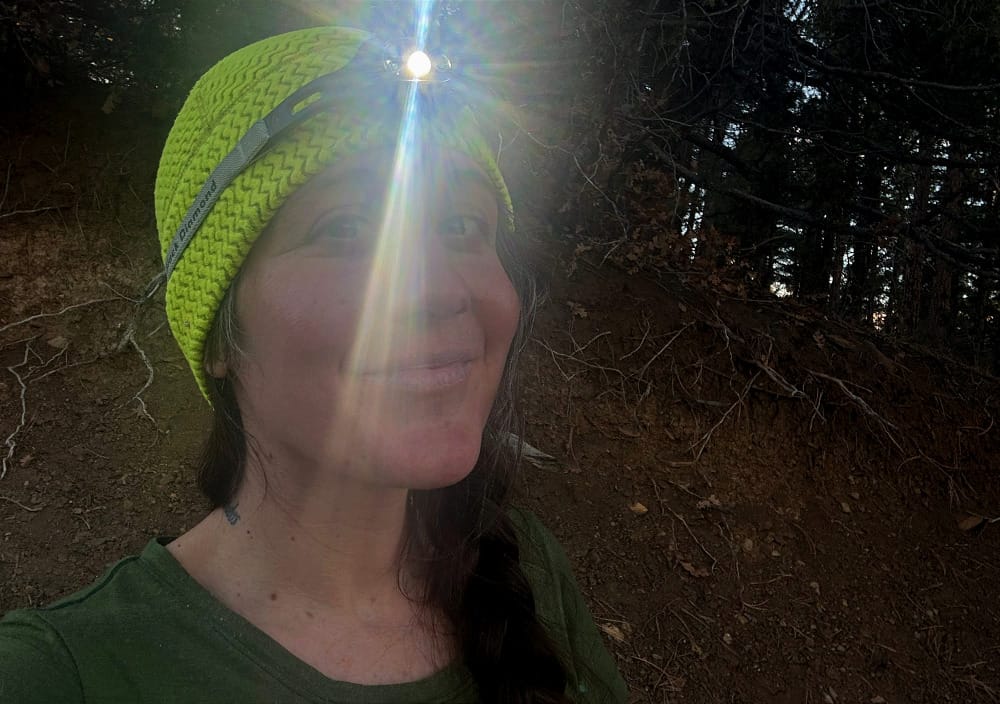 Person wearing the Black Diamond Deploy 325 headlamp in low light, demonstrating the brightness and fit of the ultralight headlamp during outdoor use.