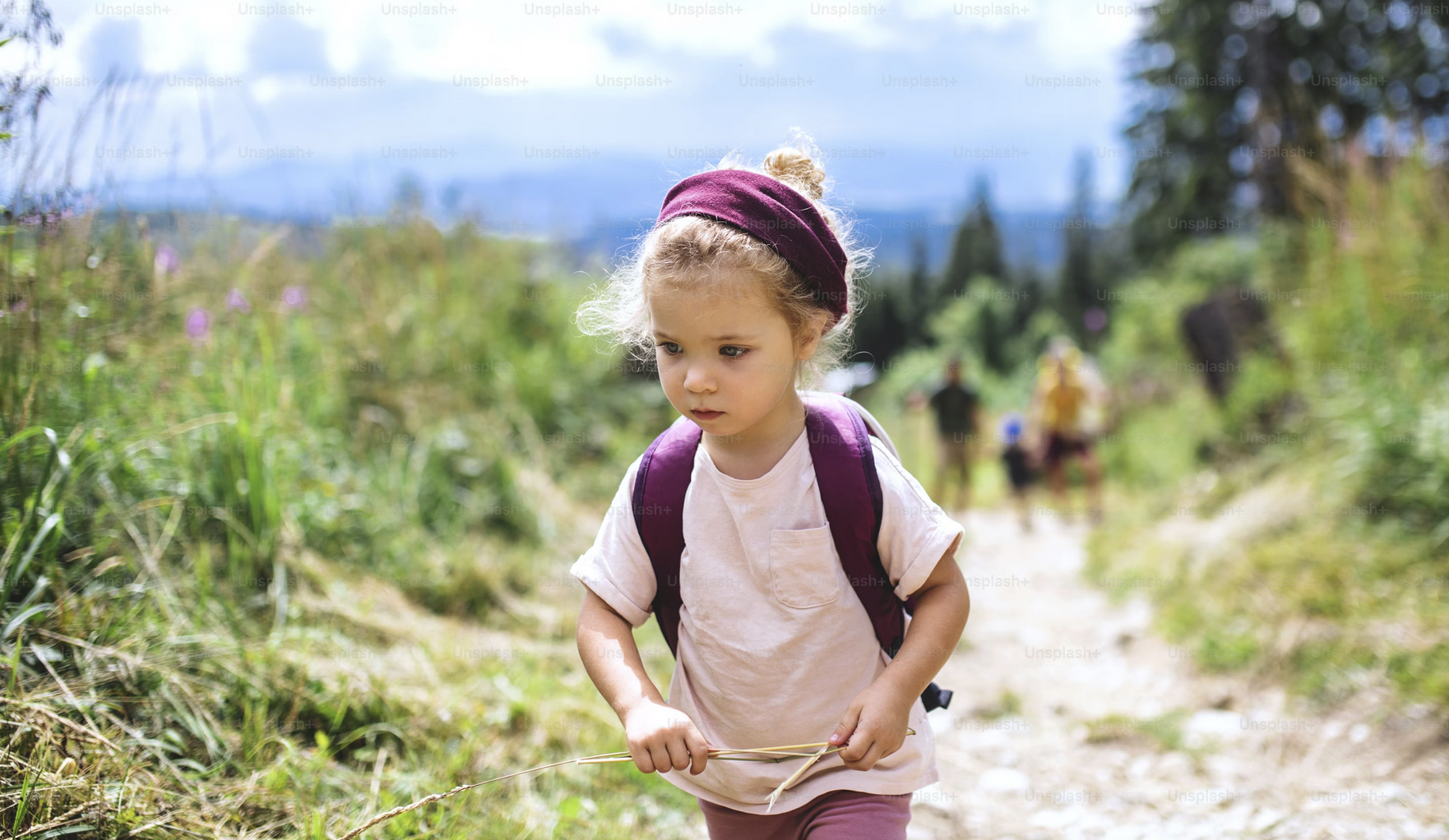 a young kid going hiking with her own backpack on a family hike