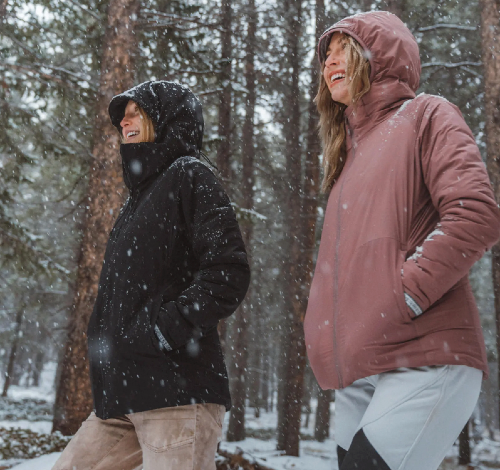 two women wear the apu pakafill lightweight puffer from paka in a snowy forest on a winter day