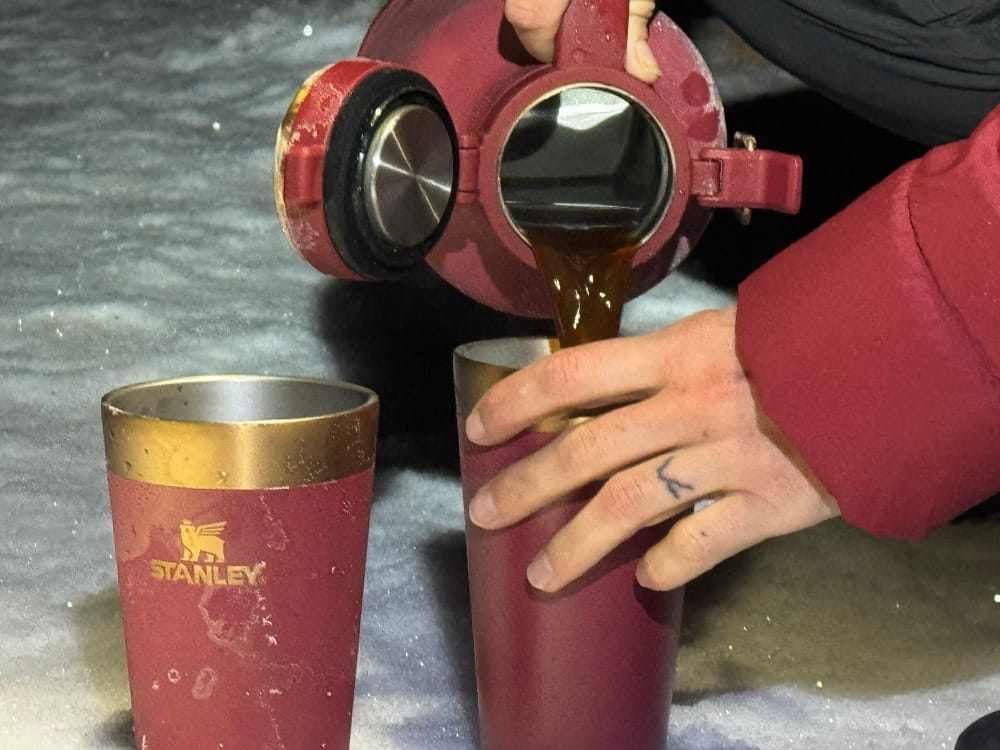 a camper pours from the Classic Easy-Pour Growler 64oz By Stanley in a snowy early morning scene