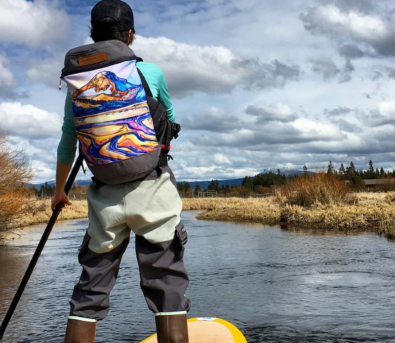 an adventurer wearing the free range equipment canvas backpack while paddle boarding in the southwest with essential gear in january