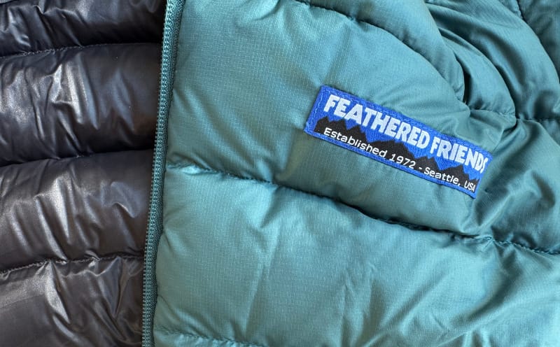 a close up of the Eos Down Jacket By Feathered Friends showing off the logo and sewn details and baffles of the down