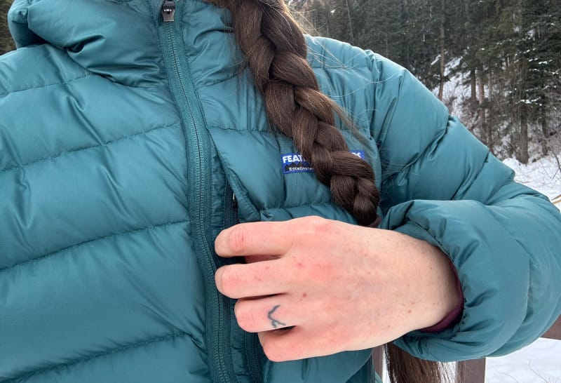 a hiker showing off the pocket on the chest of the Eos Down Jacket by Feathered Friends in a snowy scene