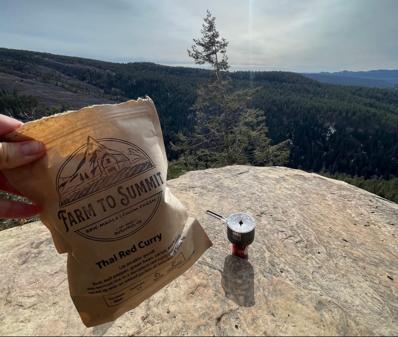 a backpacker cooking up a farm to summit dehydrated backpacking meal on the top of a mountain in colorado
