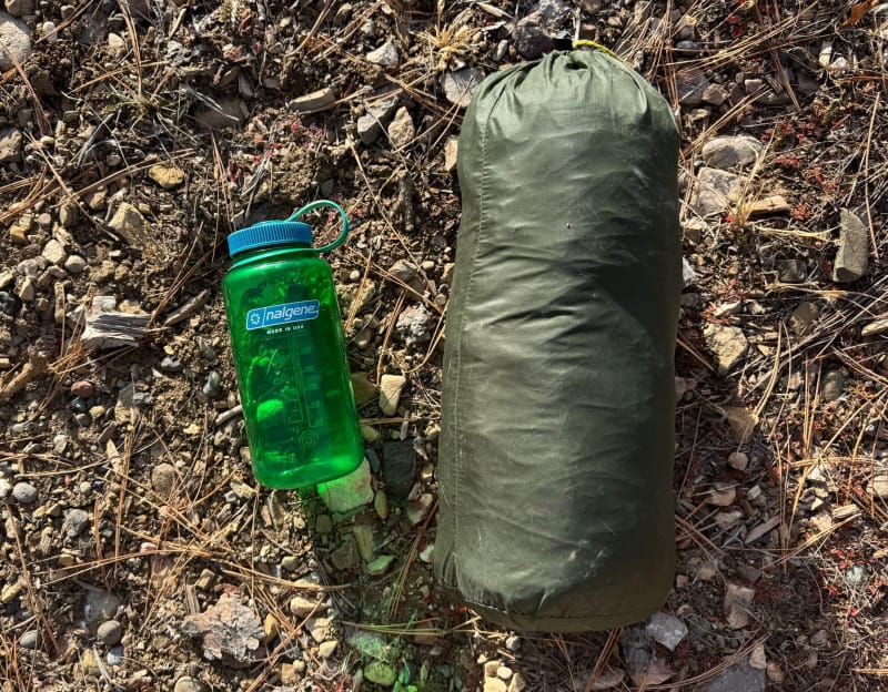 a side by side comparison of the packed up Lunar Duo Backpacking Tent By Six Moon Designs next to a nalgene bottle