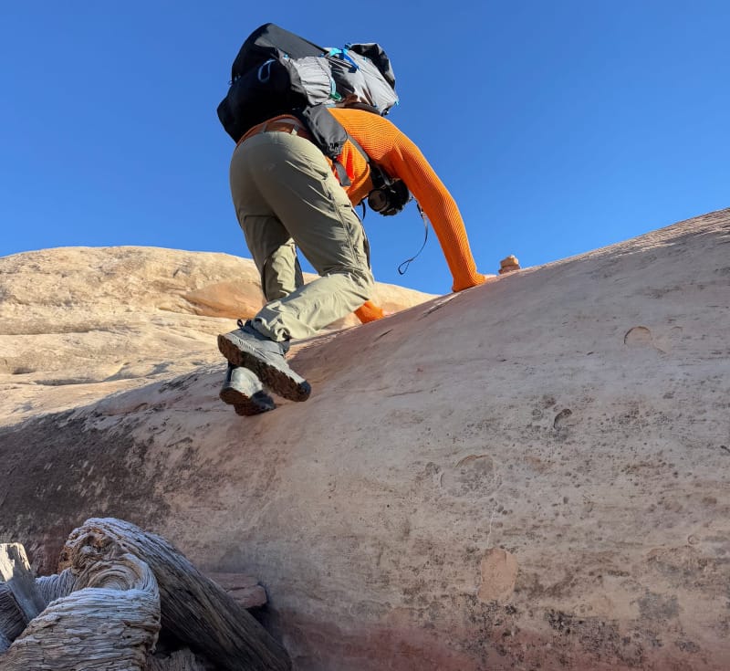 a backpacker wears the Mariposa 60 Backpack By Gossamer Gear while hiking up slick rock