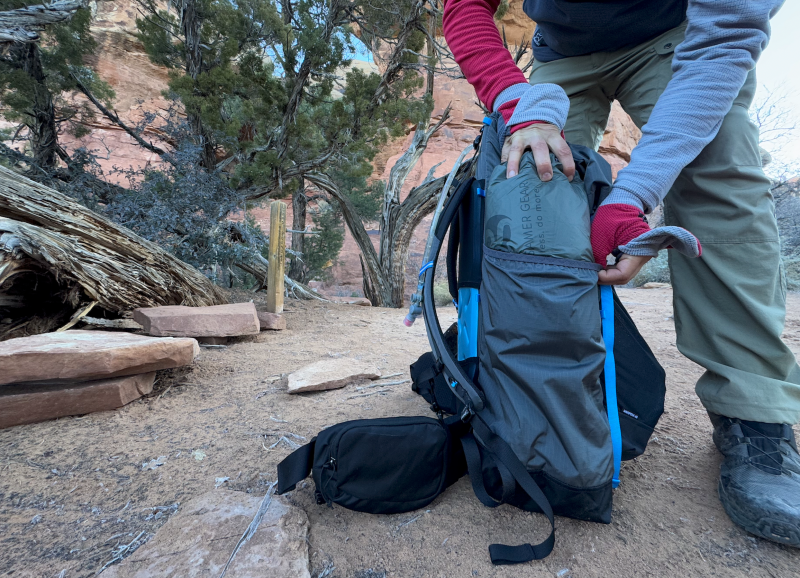 a hiker stuffs an ultralight tent into the side pocket of the Mariposa 60 Backpack By Gossamer Gear
