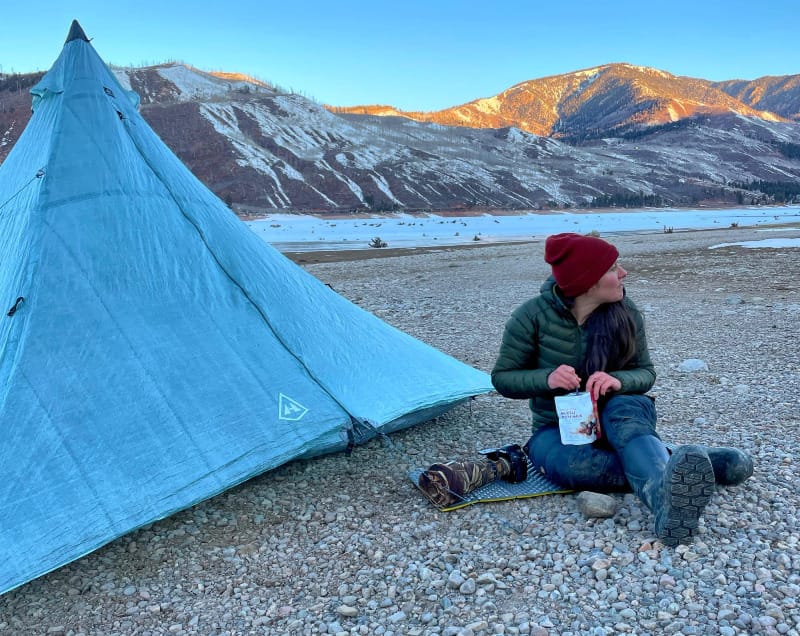 a woman on a rocky mountain beach using a UltaMid 4 Ultralight Pyramid Tent By Hyperlite Mountain Gear