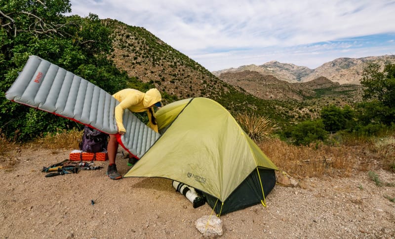 A woman setting up an ultralight tent by NEMO Equipment in a remote backcountry location, showcasing a minimalist backpacking setup.