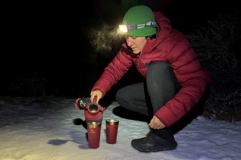A woman making camp coffee on a frigid morning while wearing the Katabatic Gear Tincup Down Jacket, showcasing its ultralight insulation for cold-weather backpacking.