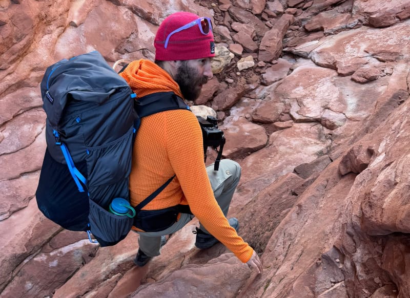 A hiker wearing a Gossamer Gear Mariposa 60 backpack while trekking through rugged backcountry, demonstrating ultralight backpacking gear in action.