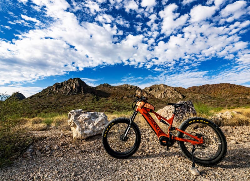 the Scout Full Suspension eBike By Bakcou in the sonoran desert on a technical 4x4 road with a mountain backdrop and dramatic sky