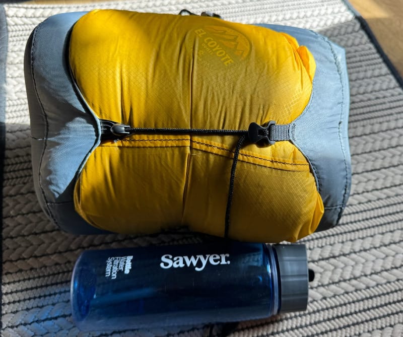 AlphaLite 900+ Custom Made Quilt By El Coyote in a compression bag sitting next to a water bottle for a size comparison of this ultralight bag