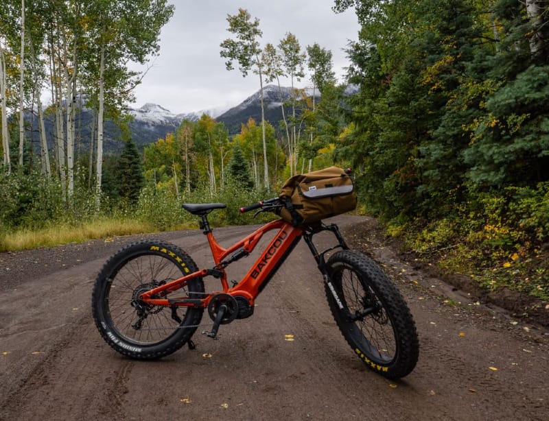 the Scout Full Suspension eBike By Bakcou on a jeep road in autumn with a backdrop of mountains. the bike is all loaded up with gear