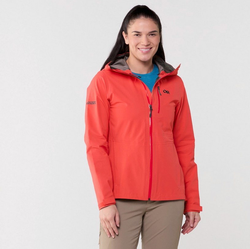 Woman wearing a coral Outdoor Research Aspire II rain jacket for women, standing against a white background.