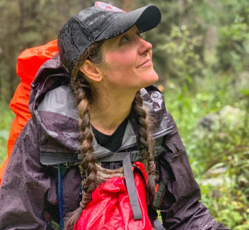 Woman wearing a rain jacket and cap while hiking in the forest during rainy weather.