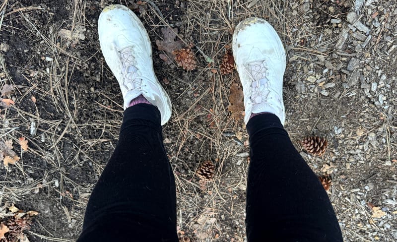  Close-up of person’s legs wearing black Branwyn Essential Compression Leggings and white trail runners on a forested dirt trail.