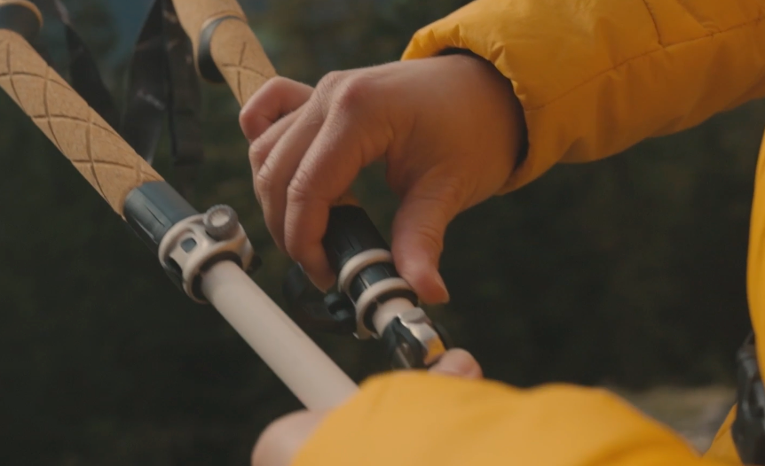  Close-up of a hiker adjusting the locking mechanism on the LEKI Cressida FX Carbon AS trekking pole with a yellow jacket in the background.