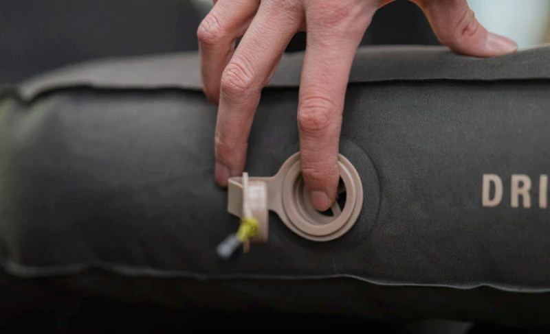  Close-up of a hand pressing the air valve on a Luno inflatable mattress during setup for car camping.