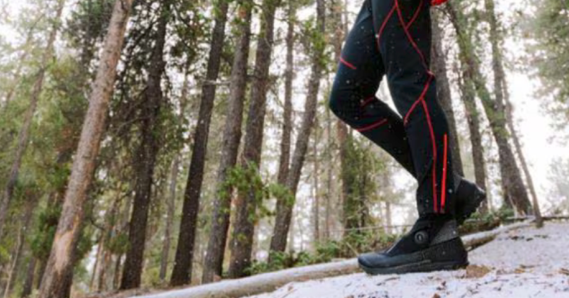  Runner wearing La Sportiva Cyklon Cross GTX shoes and black running tights in a snowy forest with light snowfall.