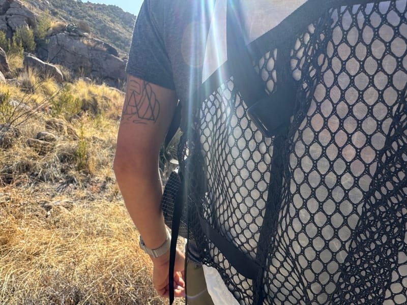  Close-up of a hiker wearing the Hyperlite Mountain Gear Windrider 40 backpack, showing black mesh pocket and strap detail in dry desert terrain.