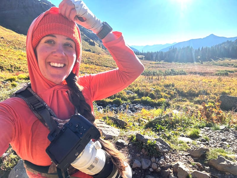  Hiker wearing an orange WURU sunshirt and camera harness, smiling in early morning alpine light with beanie under the hood.