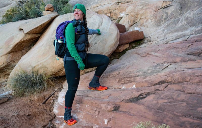  Woman wearing colorful budget-friendly hiking gear and a small pack while scrambling on sandstone.