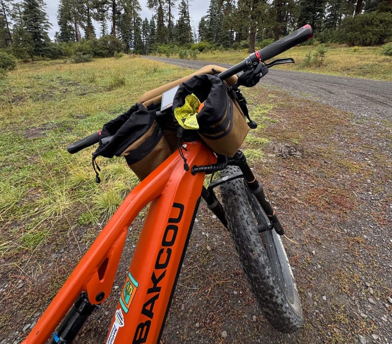 Close-up of Bakcou Scout bike’s handlebars loaded with bags on a forest road in the mountains