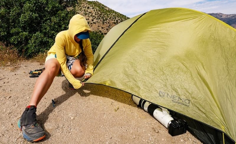 Camper pitching a budget-friendly NEMO tent on a sunny day in desert terrain.