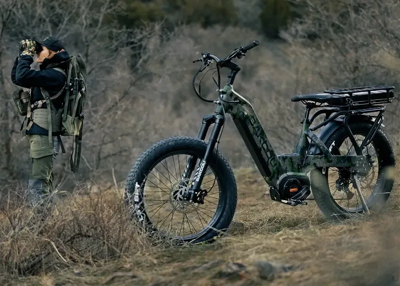 Camouflage Bakcou eBike parked beside a backpacker scanning the ridgeline with binoculars