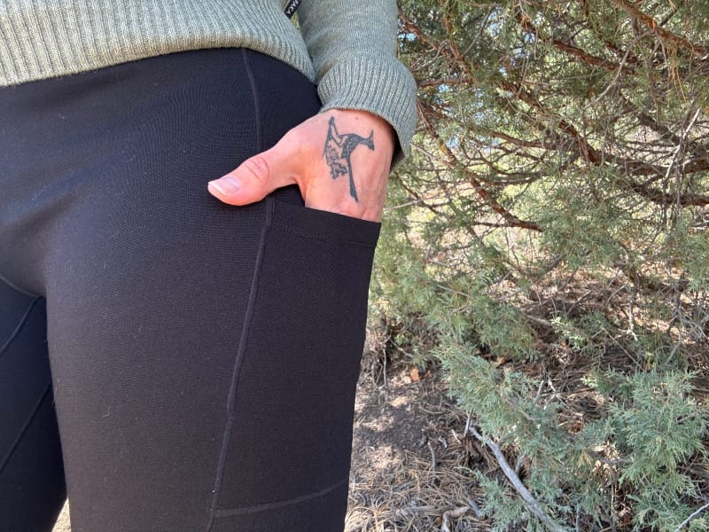  Close-up of Ibex Enduro Tights pocket showing hand and butterfly tattoo, emphasizing pocket depth and fabric texture.