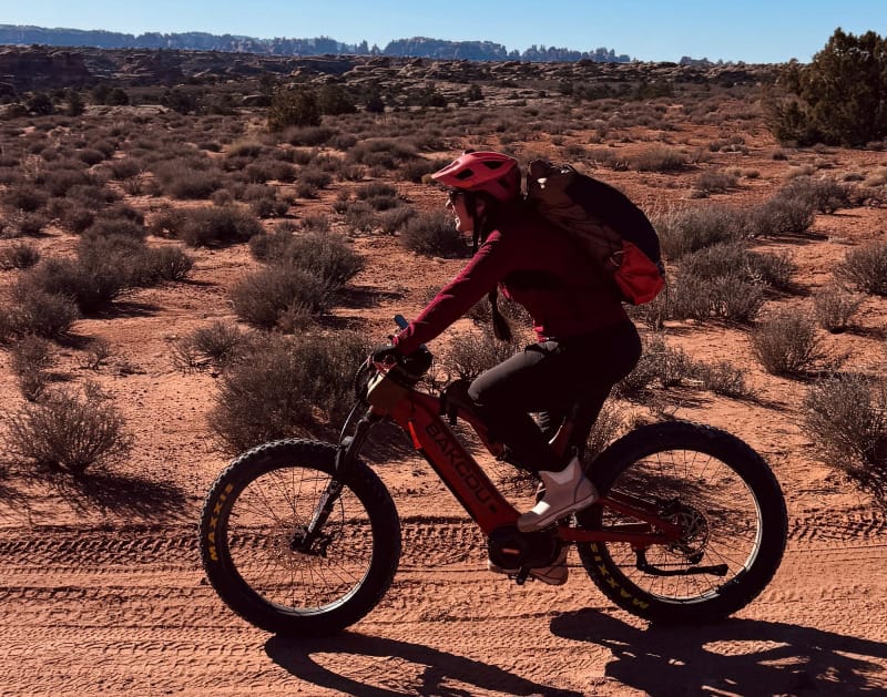 Female rider on a Bakcou eBike rides through red desert backroads with a backpack and helmet