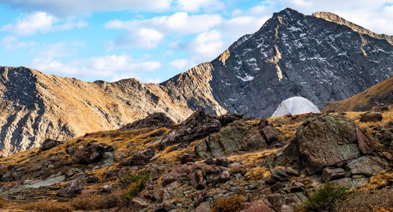 White dome-style premium tent pitched in a high alpine basin with dramatic mountain peaks in the background.
