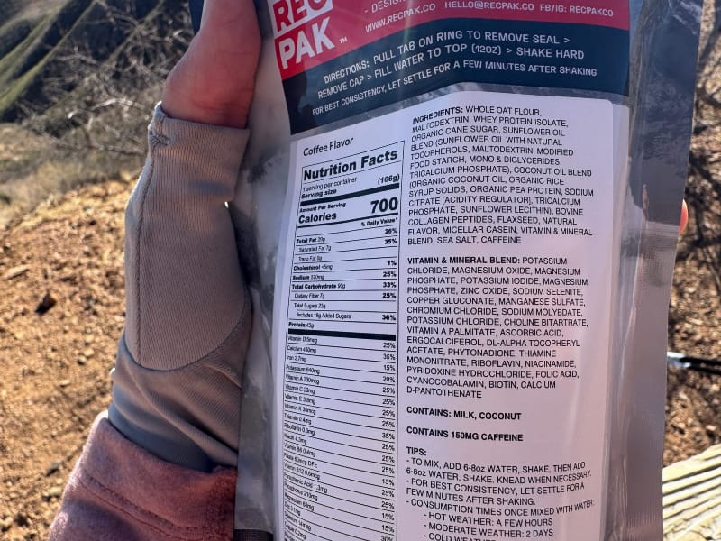  Close-up of the back of a RecPak meal pouch showing detailed nutrition facts and ingredient list, held outdoors in a sunlit desert setting.