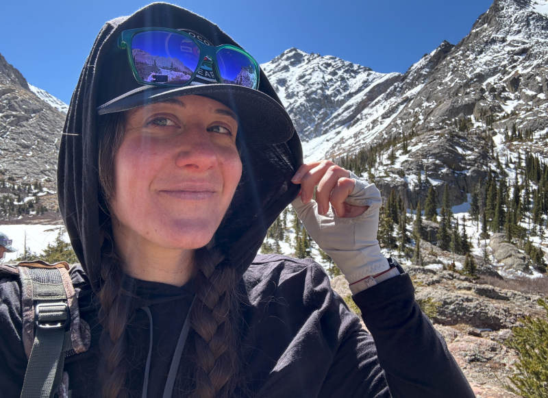  Close-up of hiker adjusting the hood of a Ridge Merino Solstice Wool Hoodie in the mountains, layered under a cap.