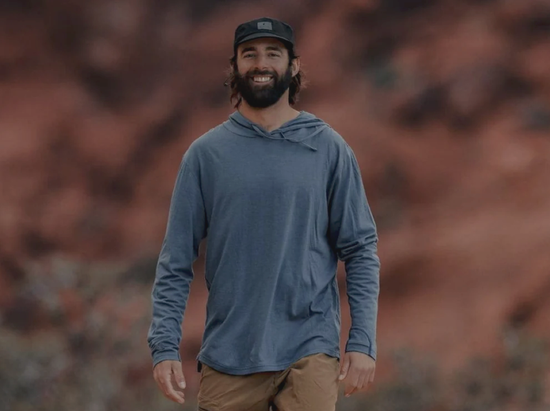  Man wearing the Ridge Merino Solstice Lightweight Wool Hoodie in a desert landscape, showcasing the relaxed fit and sun protection.