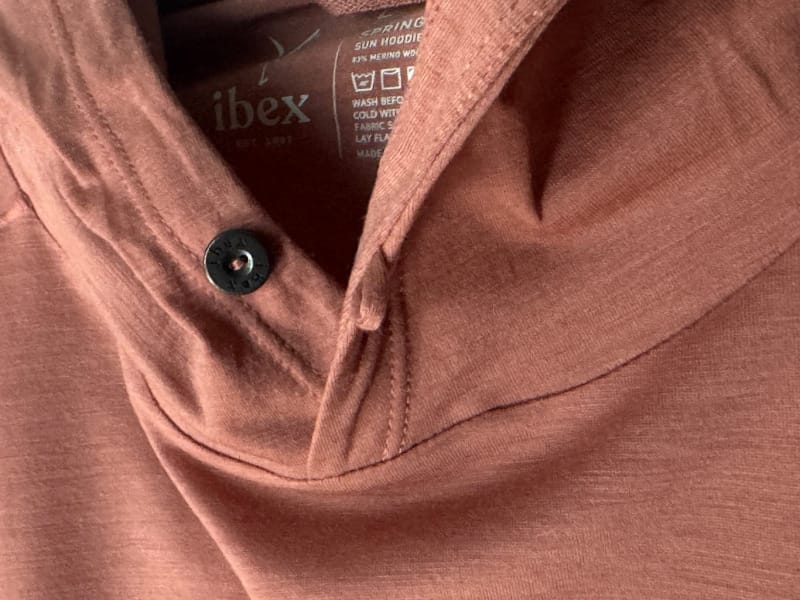 Close-up view of the Ibex Springbok Sun Hoodie fabric and button detail, showing soft merino texture and branded tag.