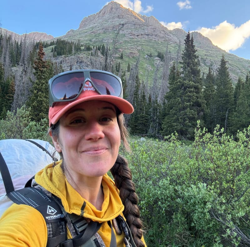 Backpacker with camera gear hiking toward mountains, carrying Feathered Friends Egret sleeping bag.
