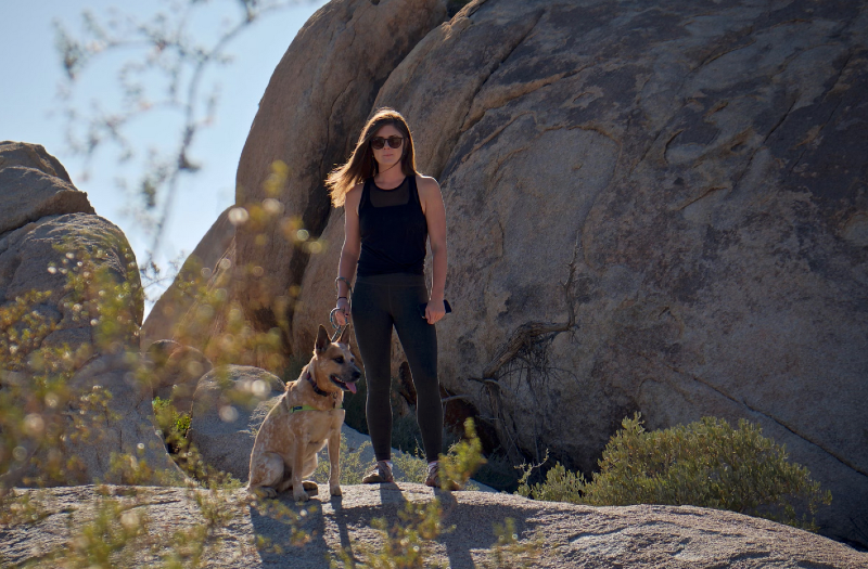 Woman hiking in a rocky desert landscape with a leashed dog standing beside her