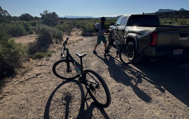  Priority 600ADX leaning near a truck as a cyclist secures another bike to a rack, with morning sun casting long shadows in the desert.