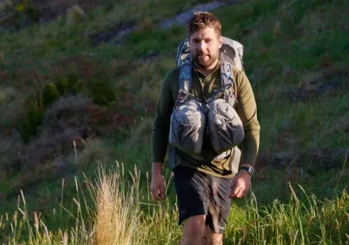  Man hiking with Aarn Mountain Magic 50 Pro backpack in grassy trail environment with balanced front and rear load