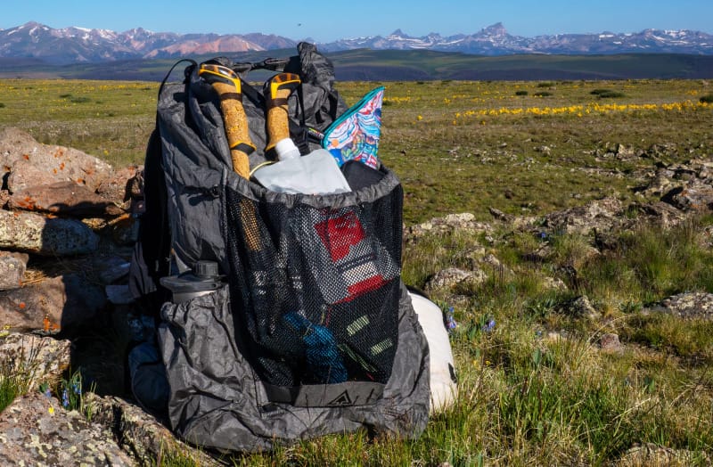  Rear view of a fully loaded Durston Kakwa 55 backpack with trekking poles and gear, set against wildflowers and the San Juan Mountains.