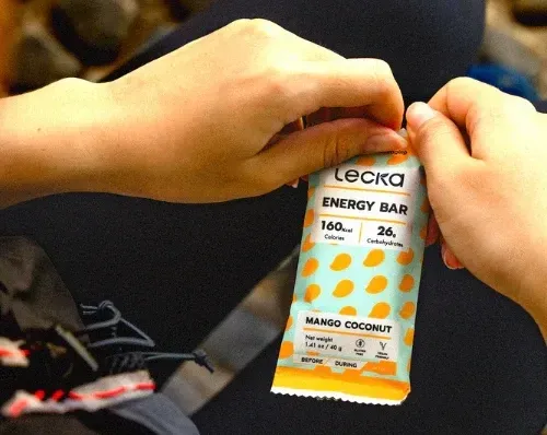 Hands opening a Mango Coconut Lecka Energy Bar while sitting outdoors, preparing for a snack break.