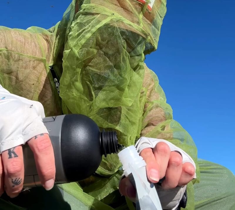  Backpacker in bug netting pouring water from a Mazama M!GO bottle into a filtration pouch in the backcountry.