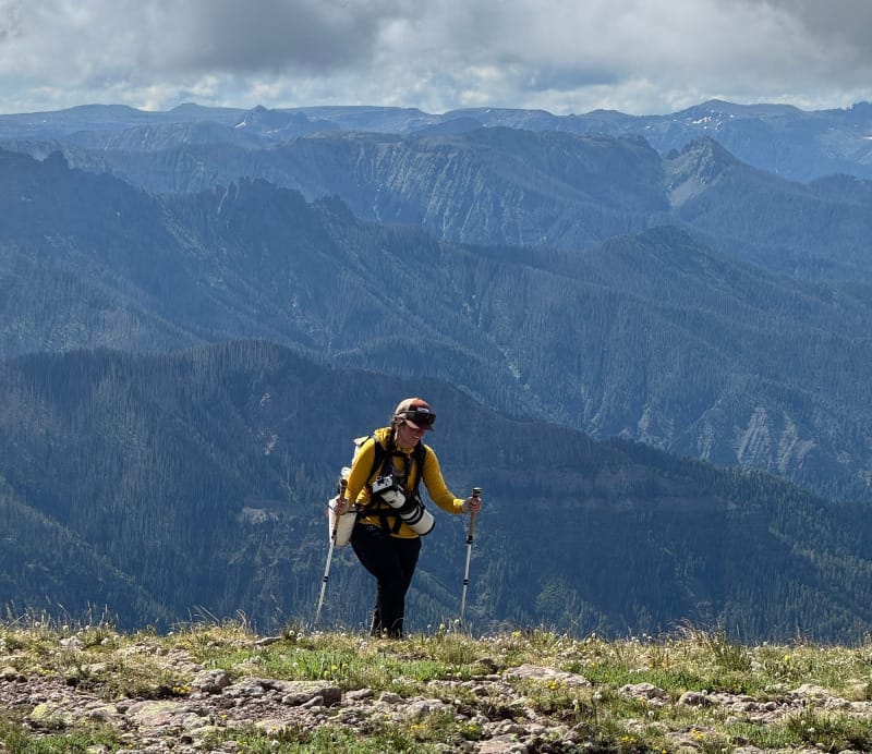 Backpacker climbing a rocky ridgeline wearing the Hyperlite Windrider 40, with mountain peaks in the background.