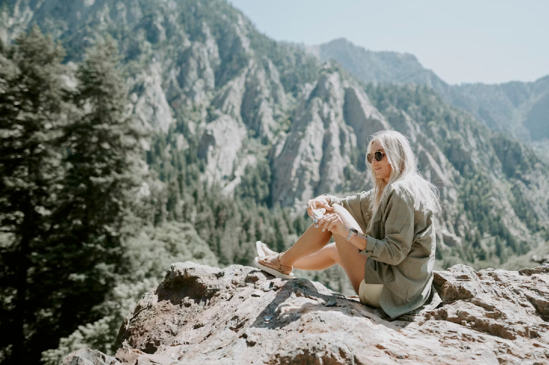 Woman sitting on a rock in the mountains enjoying a hiking break with a scenic alpine backdrop.